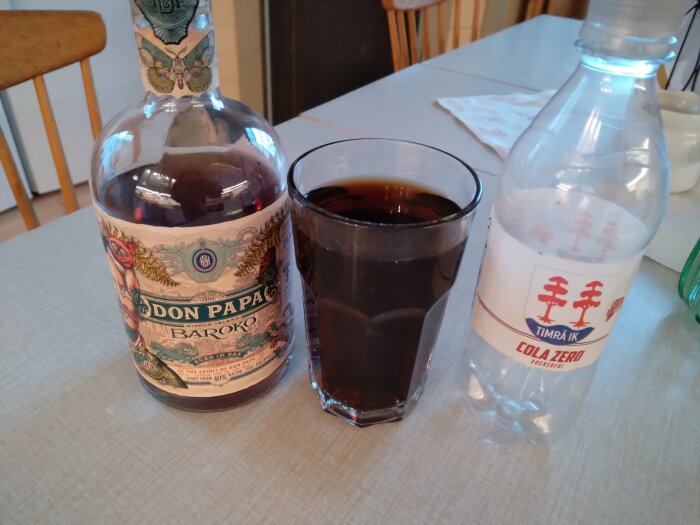 Romflaska, glas med dryck, Cola Zero-flaska, köksbord, suddig bakgrund.