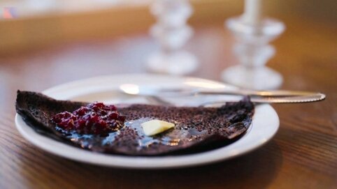 En tallrik med en halv äten pannkaka, smör, sylt, och en gaffel, på ett bord med bakgrunden suddig.