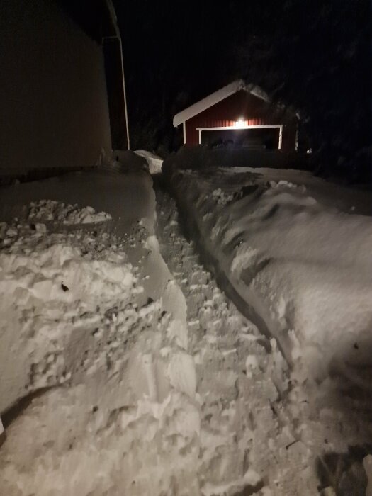 Mörk vinternatt, snötäckt väg, upplyst garage i fjärran, lugn och stilla miljö.