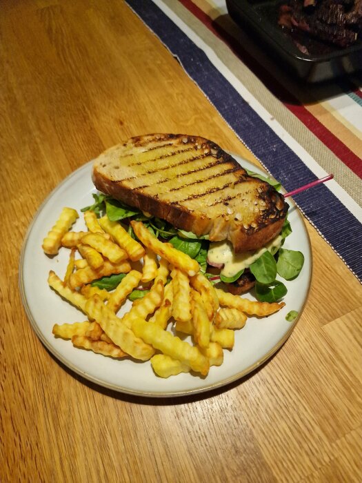 Grillad smörgås med sallad och dressing, krispiga pommes frites, på en vit tallrik, träbord.