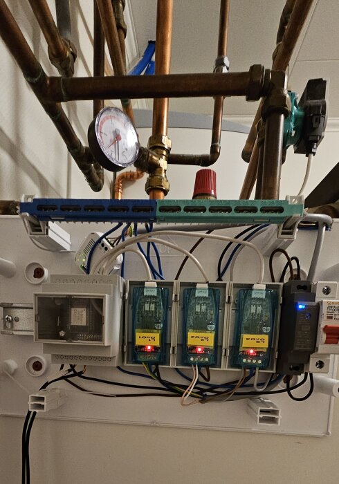 Värmesystem med rör, manometer, elektriska komponenter och mätare på vägg.