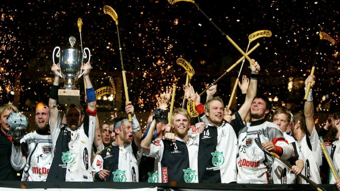 Glad ishockeylag firar med pokal och höjda klubbor, konfetti, seger, eufori, publik, mästare.