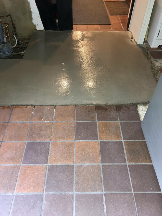 Nyligen gjuten betongplatta intill ett befintligt kaklat golv. Renovering eller reparation pågår. Inomhusmiljö.
