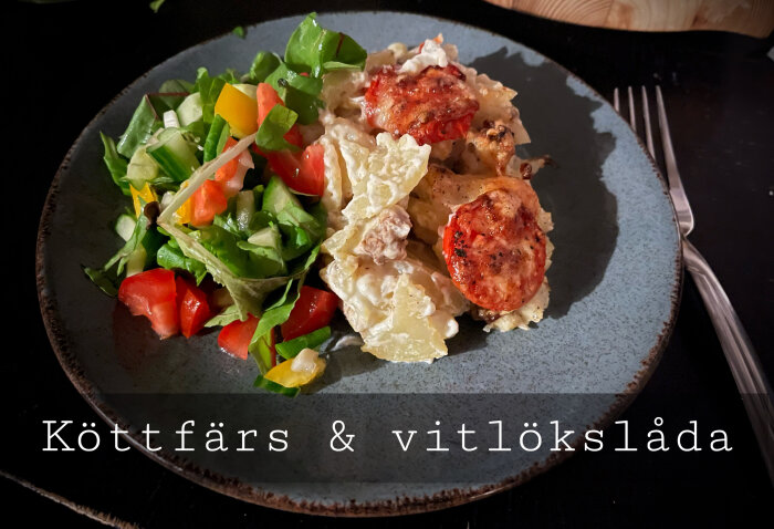 Ett måltid med gratäng och sallad på mörkblå tallrik, text "Köttfärs & vitlökslåda". Utomhus eller mörk bakgrund.