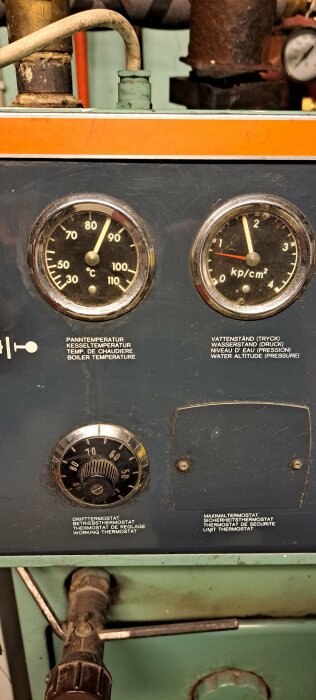 Industriell panel med mätare för temperatur och tryck, termostater, och text på flera språk.