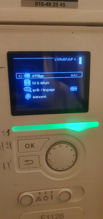 Digital kontrollpanel för värmepump med menyval på svenska, grönt ljus, navigeringsknappar och OK-knapp.