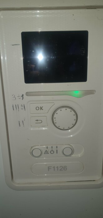 Värmepumpens kontrollpanel, smutsig, med knappar, skärm och lysande grön lampa.
