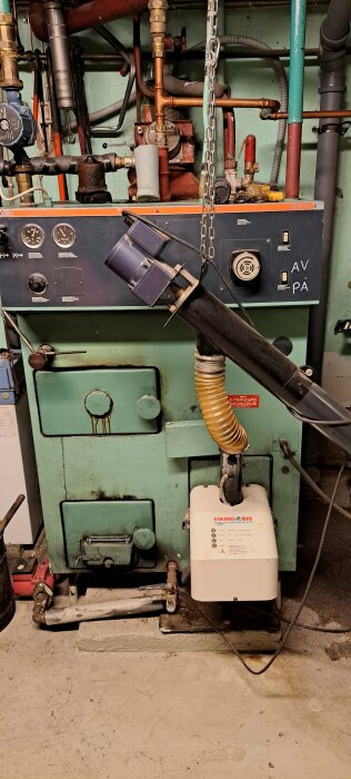 Industriell miljö med pannanläggning, rör, kablar och upplyst av lykta för arbetsbelysning.