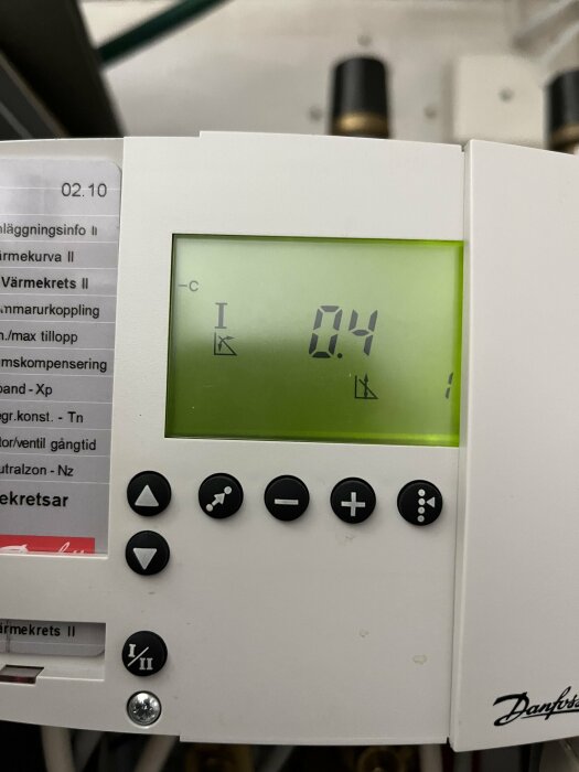 Digital termometer visar 0.4 grader Celsius, vit bakgrund, knappar, instruktionslapp, del av utrustning.