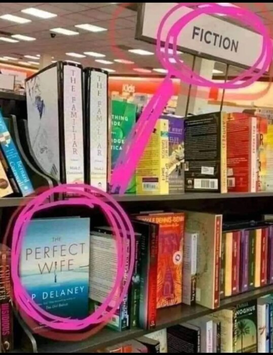 Bokhylla i butik, skylt markerar skönlitteratur, fokus på boktiteln "The Perfect Wife". Ironiskt.