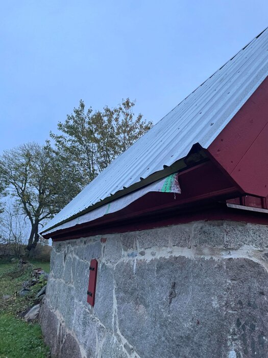 Stenhus med rött tak och detaljer, omgiven av träd i dunkelt ljus.