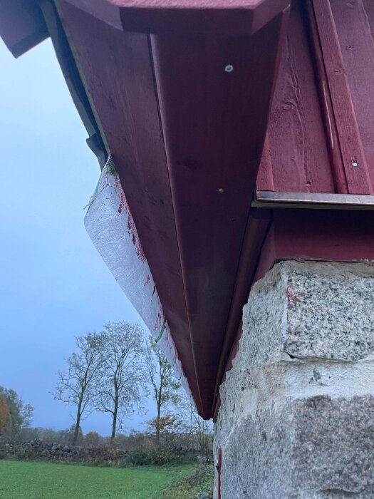 Rödfärgad byggnadskant, träkonstruktion, vit plastfilm hänger, gråsten, träd i bakgrunden, mörkt sky, utomhusvy.