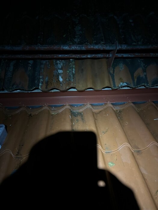 Mörk bild av ett tak med skugga från en mobiltelefon i förgrunden.