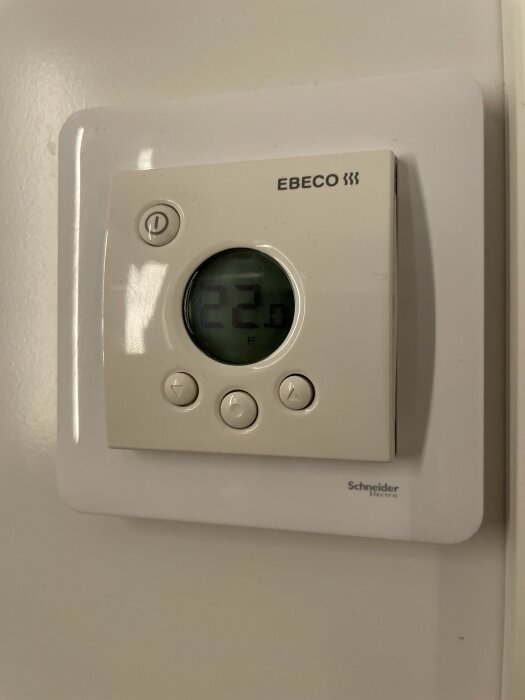 Väggmonterad EBECO termostat med digital display som visar 22.3 grader, knappar och Schneider Electric logo.