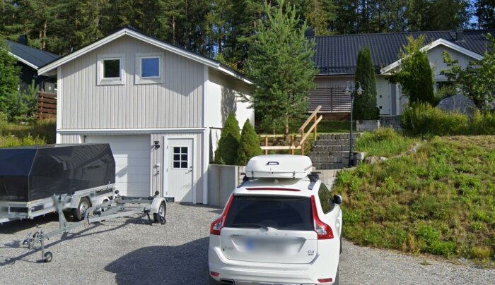 En vit bil med takbox, släpvagn, villa i förorten, grönska och soligt väder.
