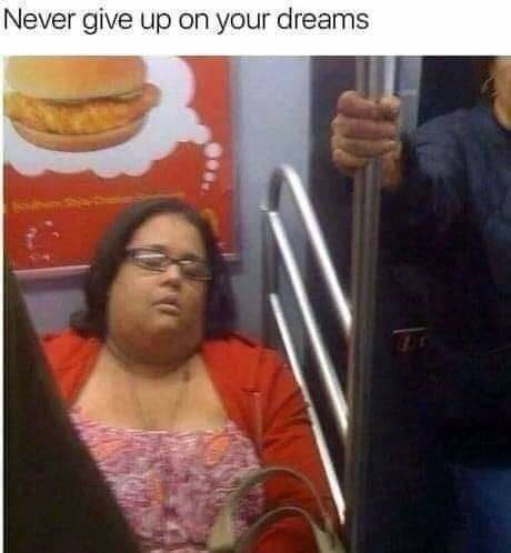 Kvinna sover på kollektivtrafik. Reklamskylt av en hamburgare ovanför. Text: "Never give up on your dreams".