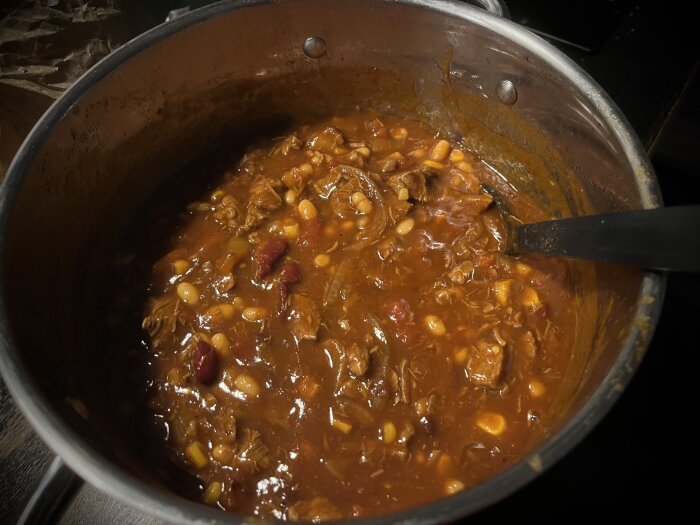 Ett gryta med chili con carne i en kastrull på ett mörkt underlag.