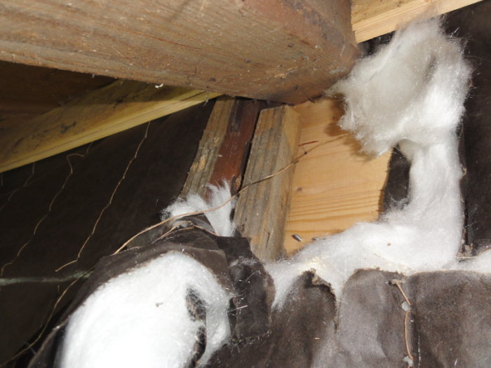 Attic view showing exposed wooden beams and insulation materials, with additional wood pieces for structural evaluation.