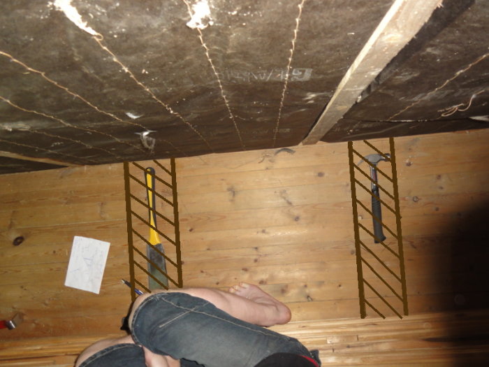 View of a construction site with wooden flooring, showing tools and insulation, and a person's legs in the foreground.