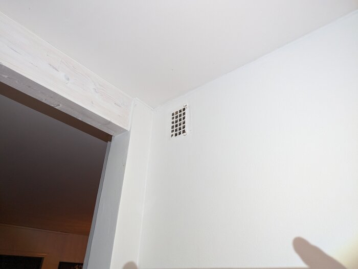 Vitrum med ventilationsgaller i hörnet, träbjälke, skuggor, inomhusbelysning.