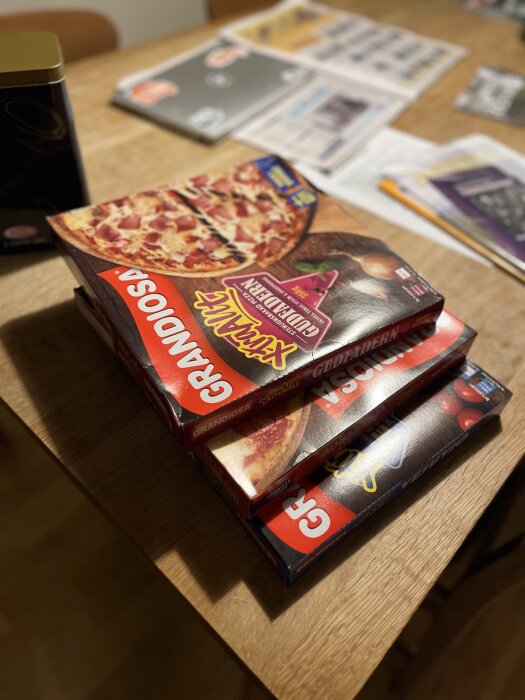 Fyra frysta pizzakartonger på ett bord med tidningar och en burk i bakgrunden.