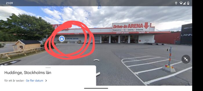 Byggvaruhus med skylt "Drive-In Arena", parkering, molnig himmel, träkonstruktion till vänster, Huddinge, Sverige.