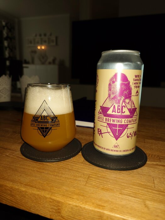 Ölglas och burk från Apex Brewing Company på ett bord, med heminredning i bakgrunden.