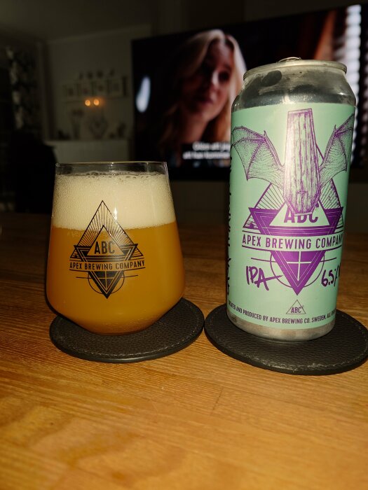 Ölglas och burk från Apex Brewing Company på bord framför TV.