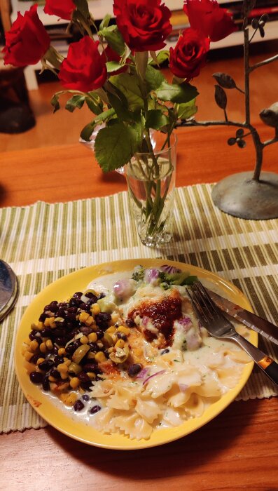 Middagstallrik med pasta, sås, och bönor-corn-blandning vid sidan, rosbukett i bakgrunden, hemtrevlig atmosfär.