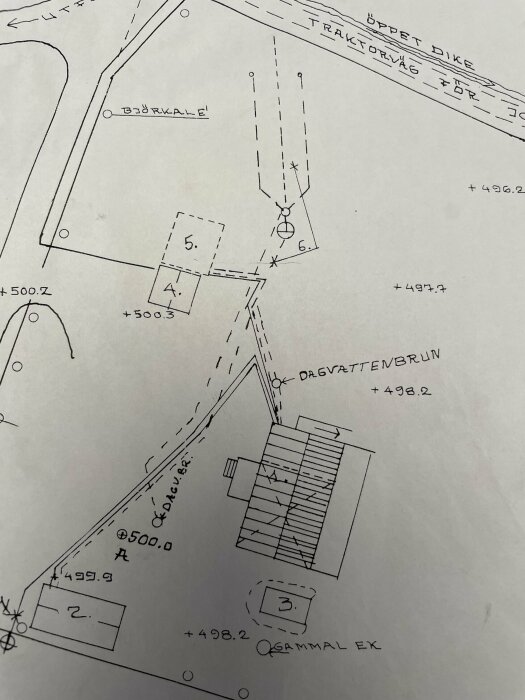 Teknisk ritning med höjdkoter, byggnader, traktorväg och naturföremål som träd och diket.
