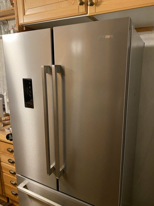 Ett stort rostfritt stål kylskåp med frysdel, modern design, i hemmiljö, med träskåp ovanför.