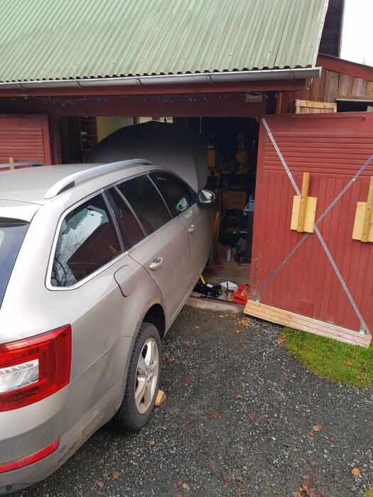 Bil körde in i garage, garageport skadad, verktyg synliga, röd dörr, rörig, träbitar används som hjulstöd.