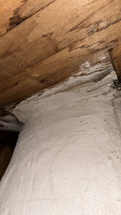 Träbjälklag och vitputsad murad yta med synligt slitage och ålderns tecken. Struktur och materialdetaljer är tydliga.