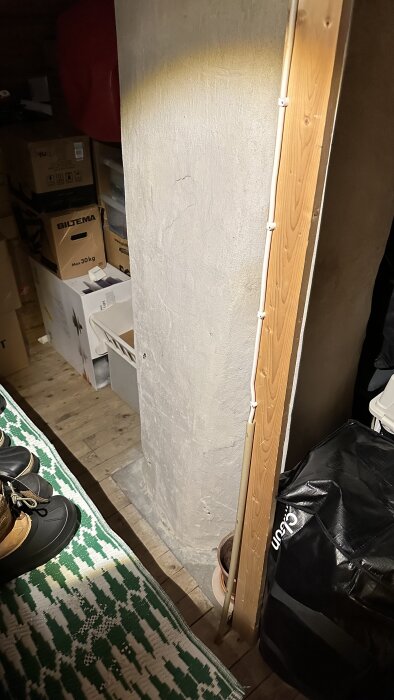 Källarutrymme med föremål, skor, lådor, grönt-mönstrad matta, ouppackad julgran och en betongvägg.