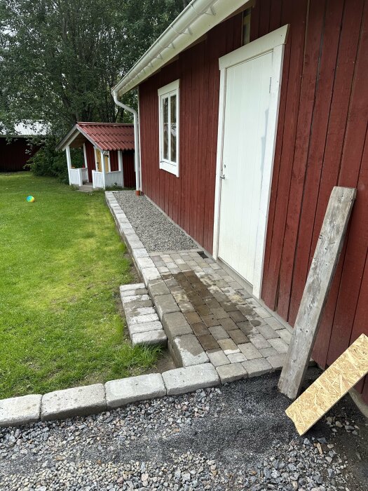 Traditionellt svenskt rött hus med vita knutar, stenstig, gräs och leksak på gräsmattan.