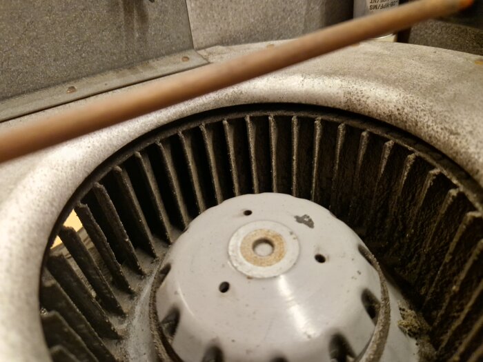 Närbild på en dammig, metallisk maskindel med ventileringsgaller och en central vit del.