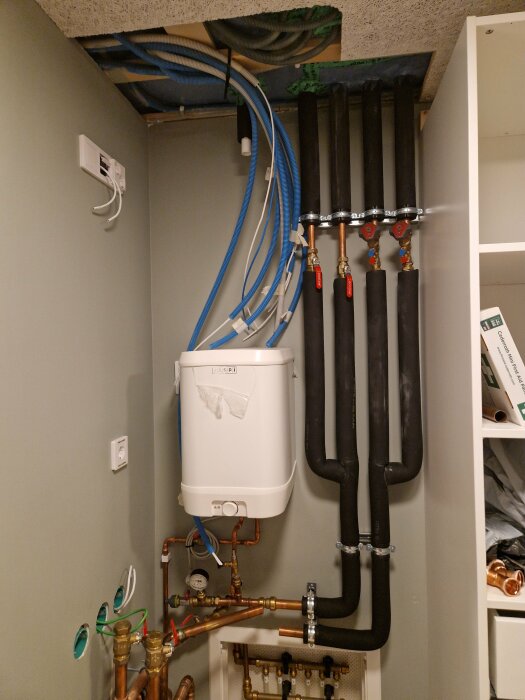 Ventilationssystem och VVS-installationer i ett förråd med rör, värmeväxlare och elektriska kablar.