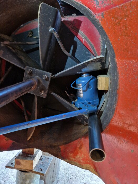 Inre del av röd cementblandare med metallvingar, blå motor och träkloss för stöd. Industriellt, använd, byggutrustning.