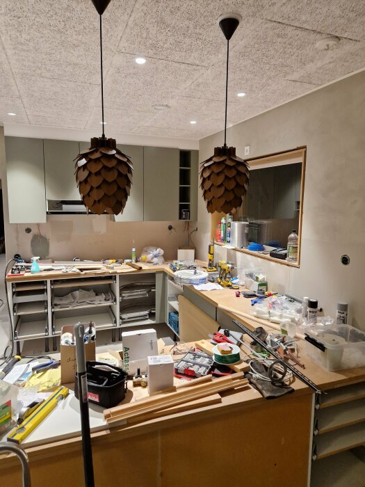 Kök under renovering, oorganiserat, verktyg och material överallt, två hänglampor, spegel och ingen bänkskiva.