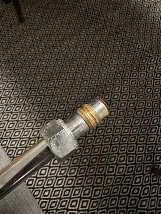 Transparent rör med metallanslutning mot grafiskt mönstrad matta.