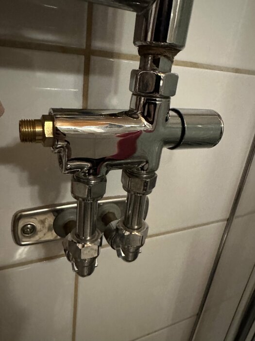 Metallisk blandningsventil, två anslutningar, badrumsinstallation, klinker i bakgrund, reflektion, ingen vattenskada synlig.