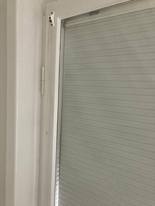 Vit dörrkarm och stängd grå rullgardin i ett rum.