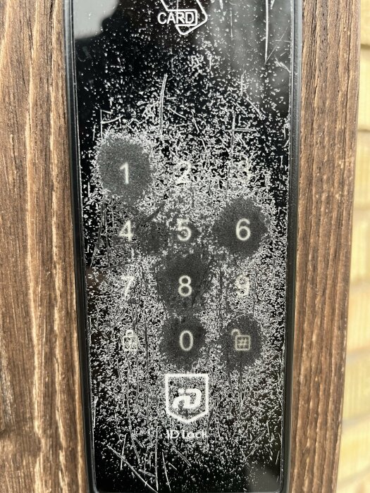 Ett dörrlås med siffertangentbord täckt av frost, utomhus, synliga fingeravtryck, kallt väder, nummer "1", "4", "5" mest använda.