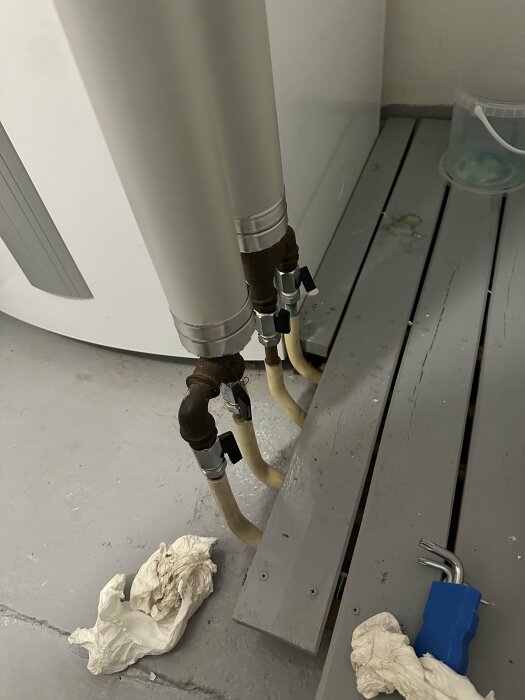 Tvättstugeutrymme med anslutna rör, använda trasor på golvet och skenor för gardiner eller skiljeväggar.