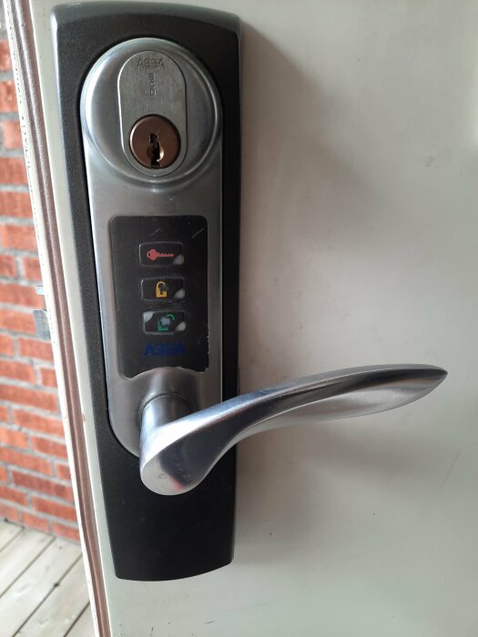 Elektronisk dörrhandtag med kodlås och nyckelhål, monterat på en vit dörr.