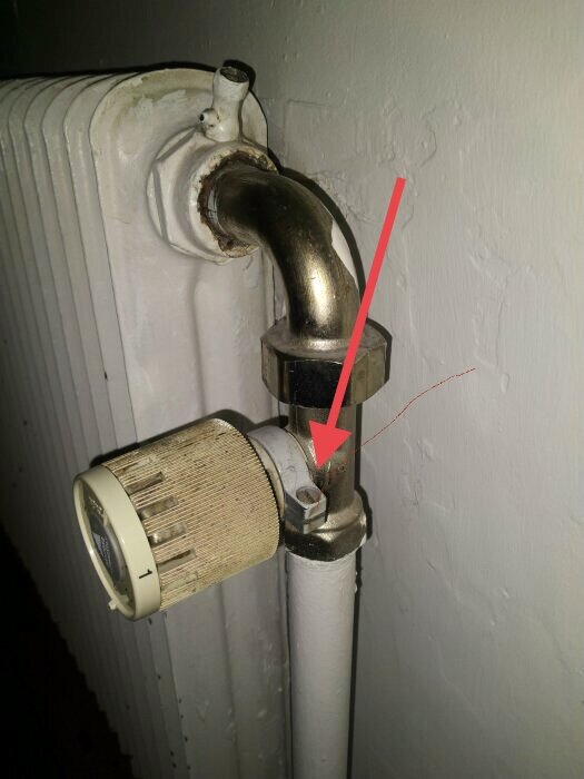 En termostatventil på en radiator med en röd pil som pekar mot en skruv.