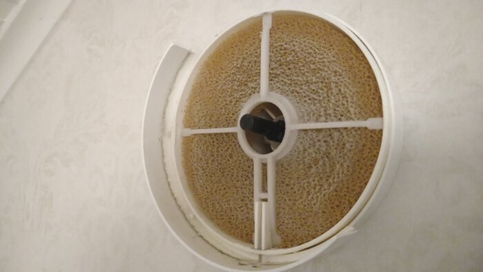 Ett kaffefilter fyllt med använd kaffesump i en vit behållare på ljust underlag.