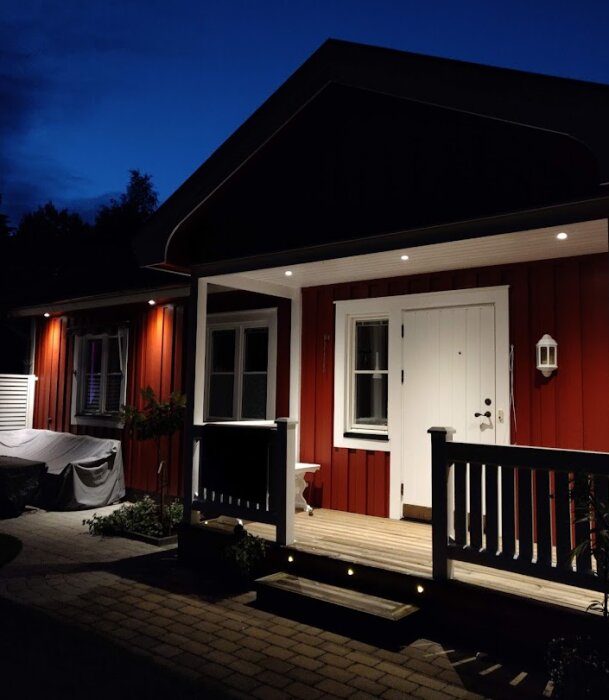 Rödmålat trähus med veranda i kvällsbelysning mot en mörkblå himmel.