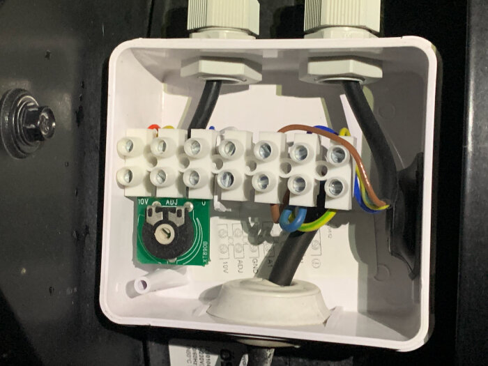 En öppen elektrisk anslutningsbox med kablar, terminalskruvar och en möjlig spänningsjusterare.