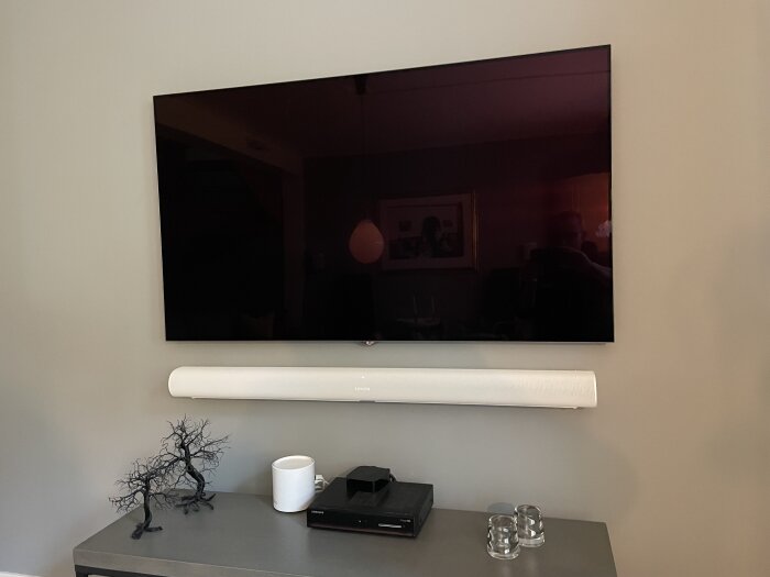 En släckt TV, ljudlimpa, dekorativ trädskulptur, kopp, två glas, reflektion av ett rum.